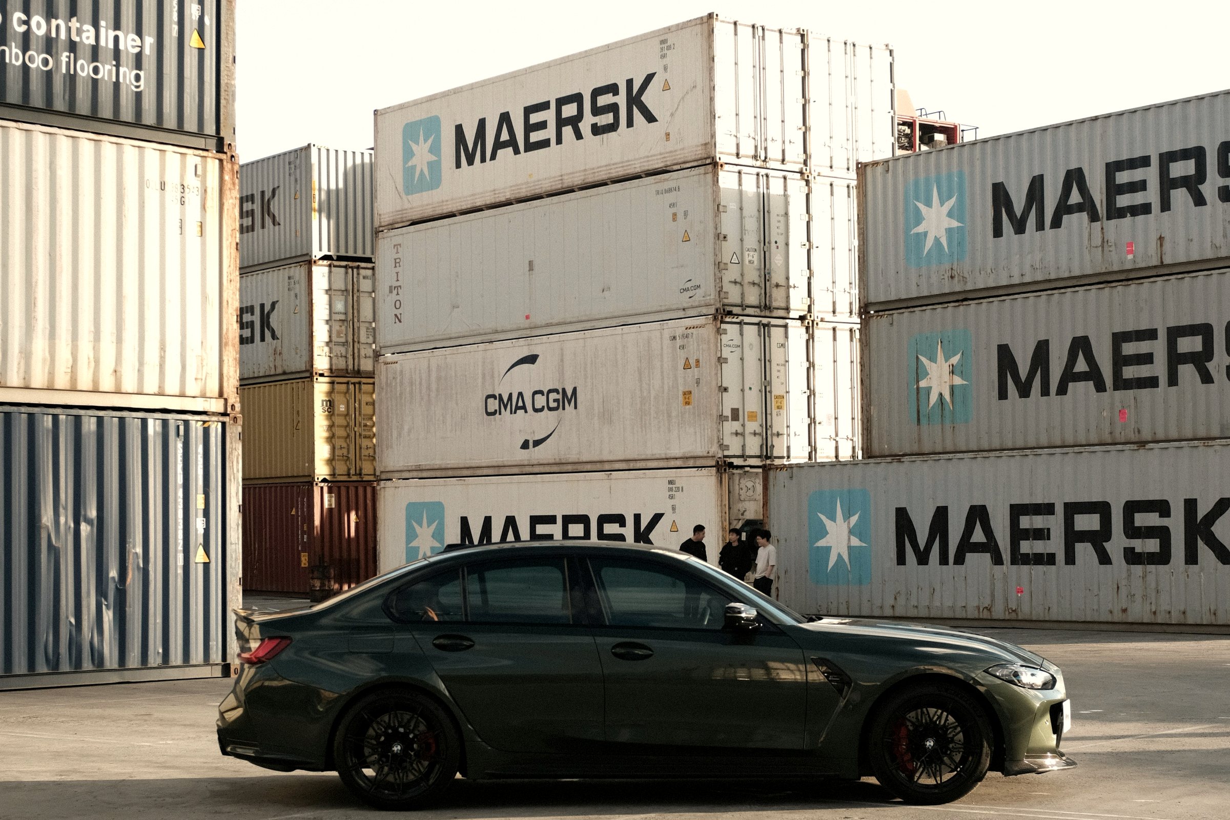 A car parked in front of stacked shipping containers at a marine terminal